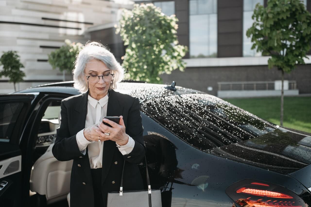 Business executive standing beside her car while using her smartphone