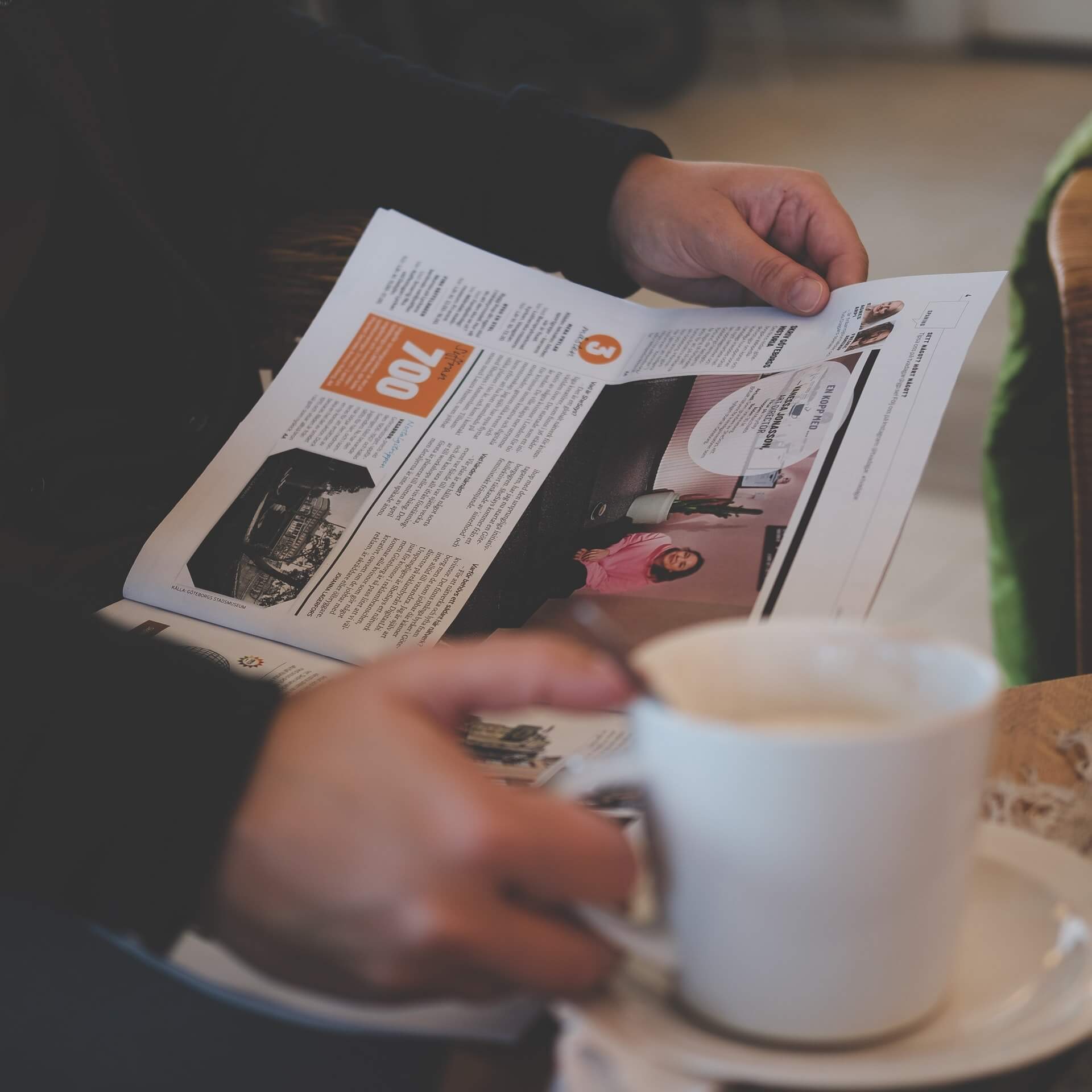 Person reading a newspaper while holding a mug