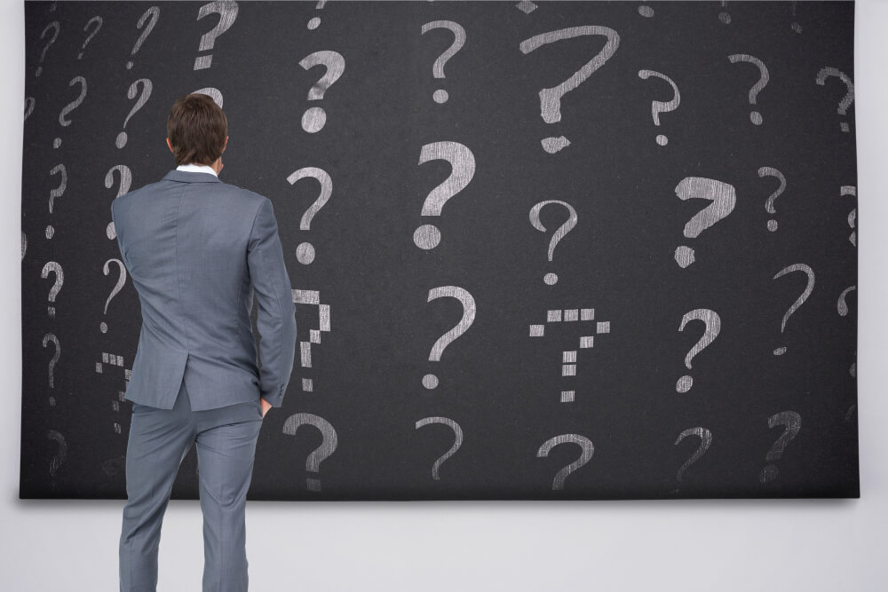 Businessman looking at question marks on a black board