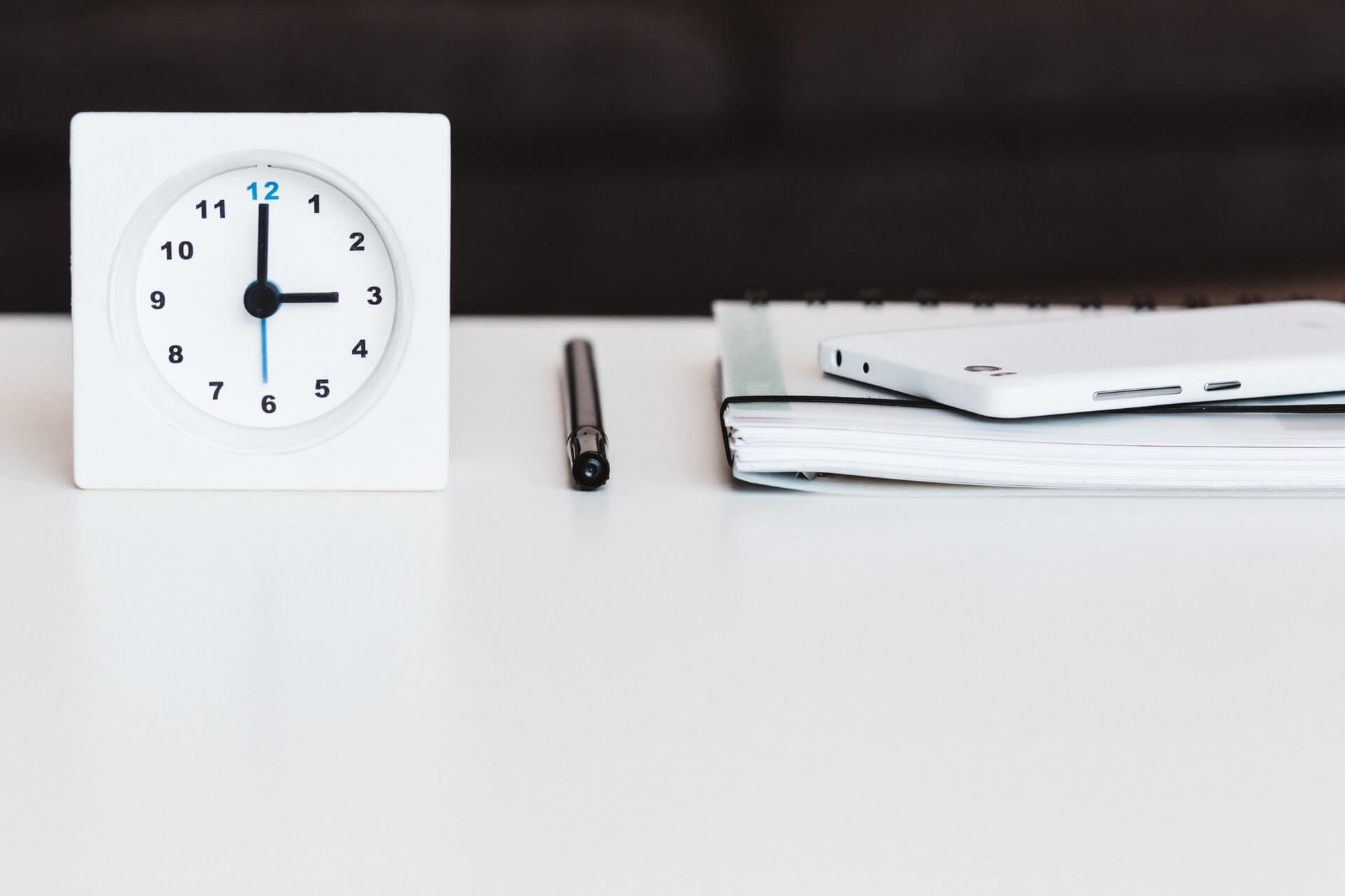 Desk clock beside a note and black pen on a table