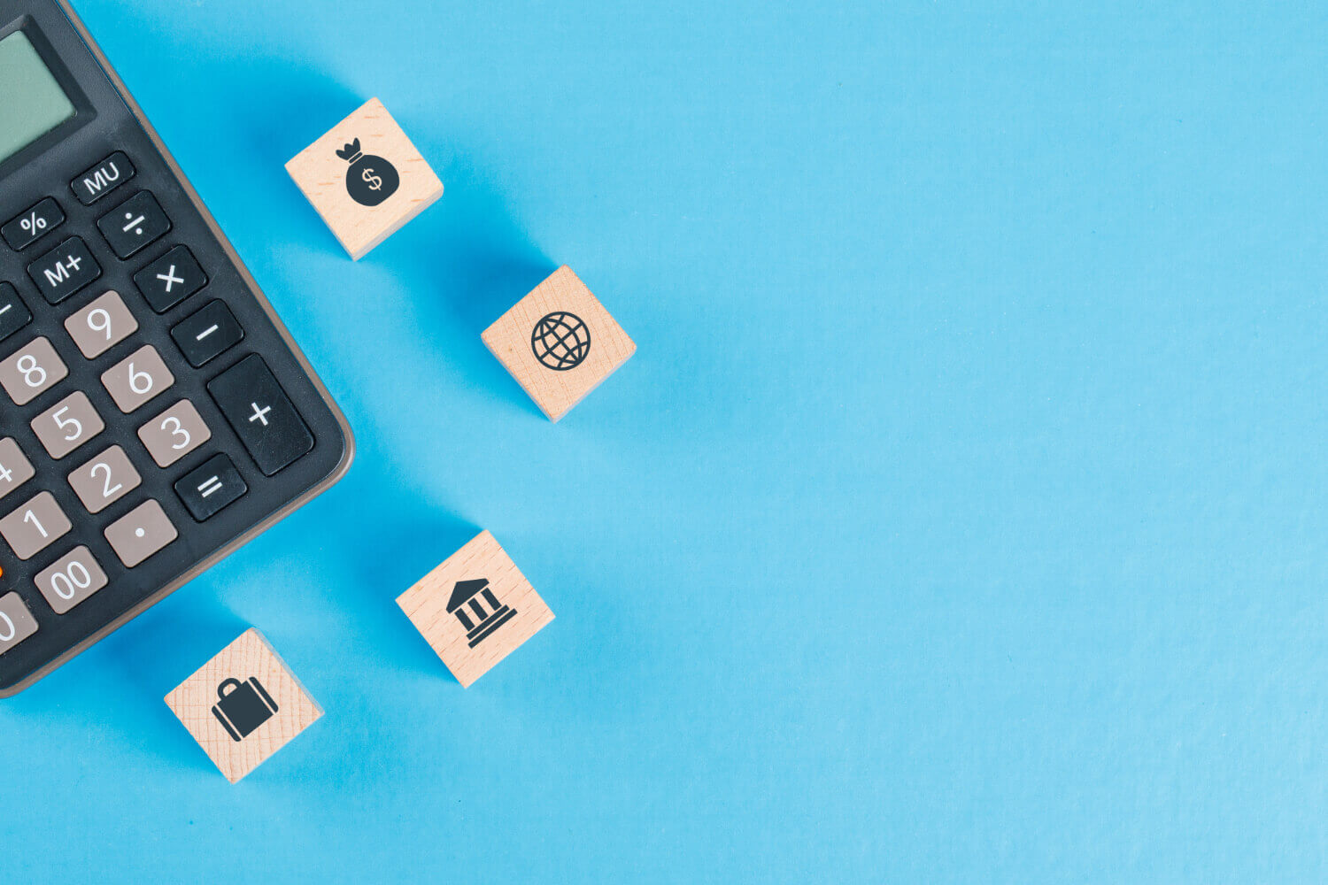 Financial concepts icons illustrated on wooden cubes and a calculator on a blue surface