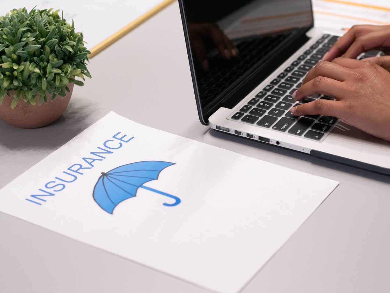 Person working on a laptop beside a paper illustrating an insurance concept