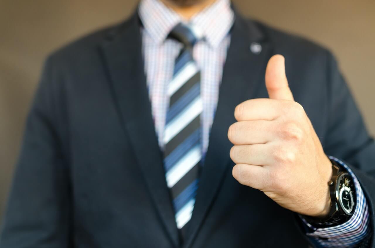 Man in black suit jacket making a thumbs up