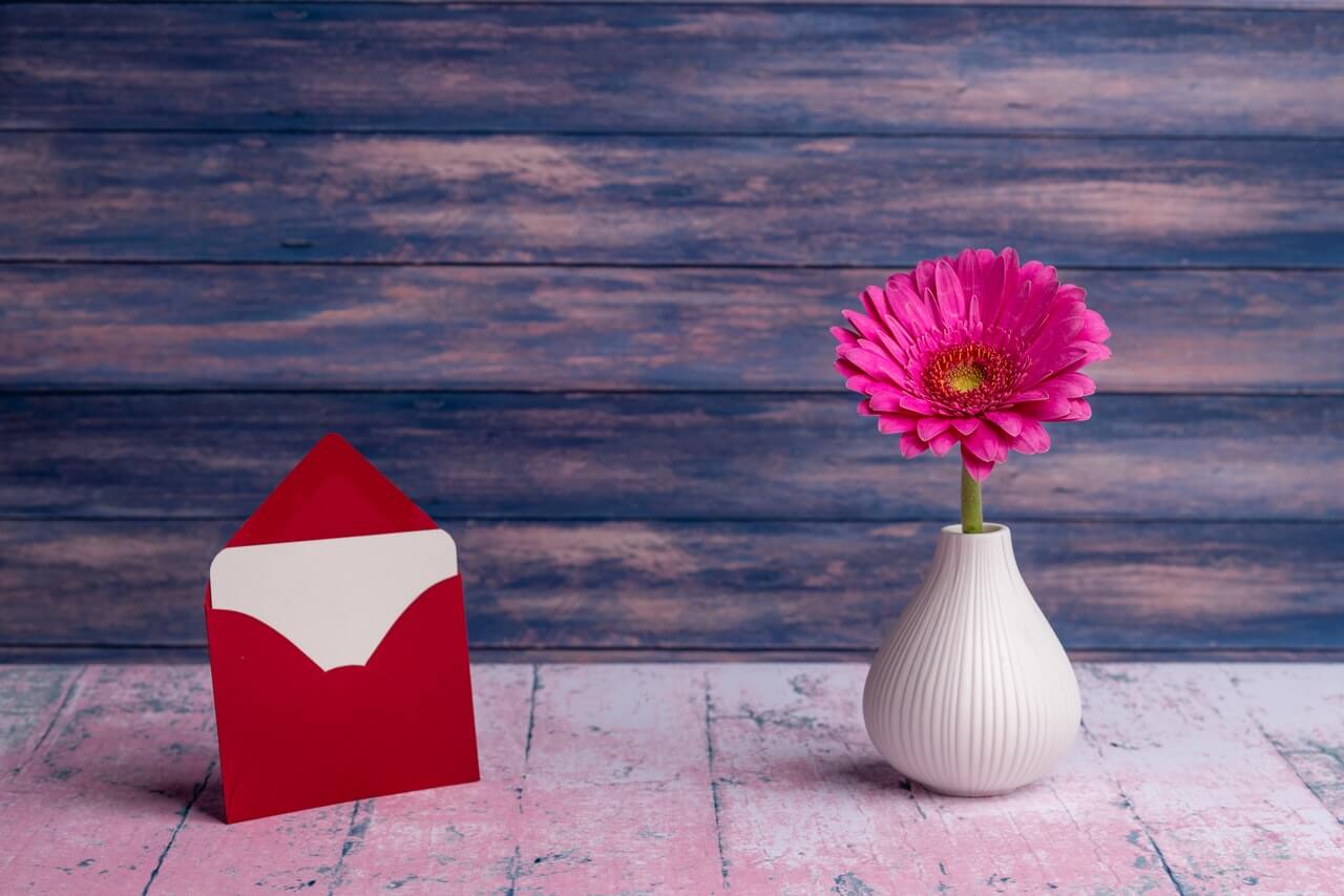 A letter in an envelop beside a small vase on a desk