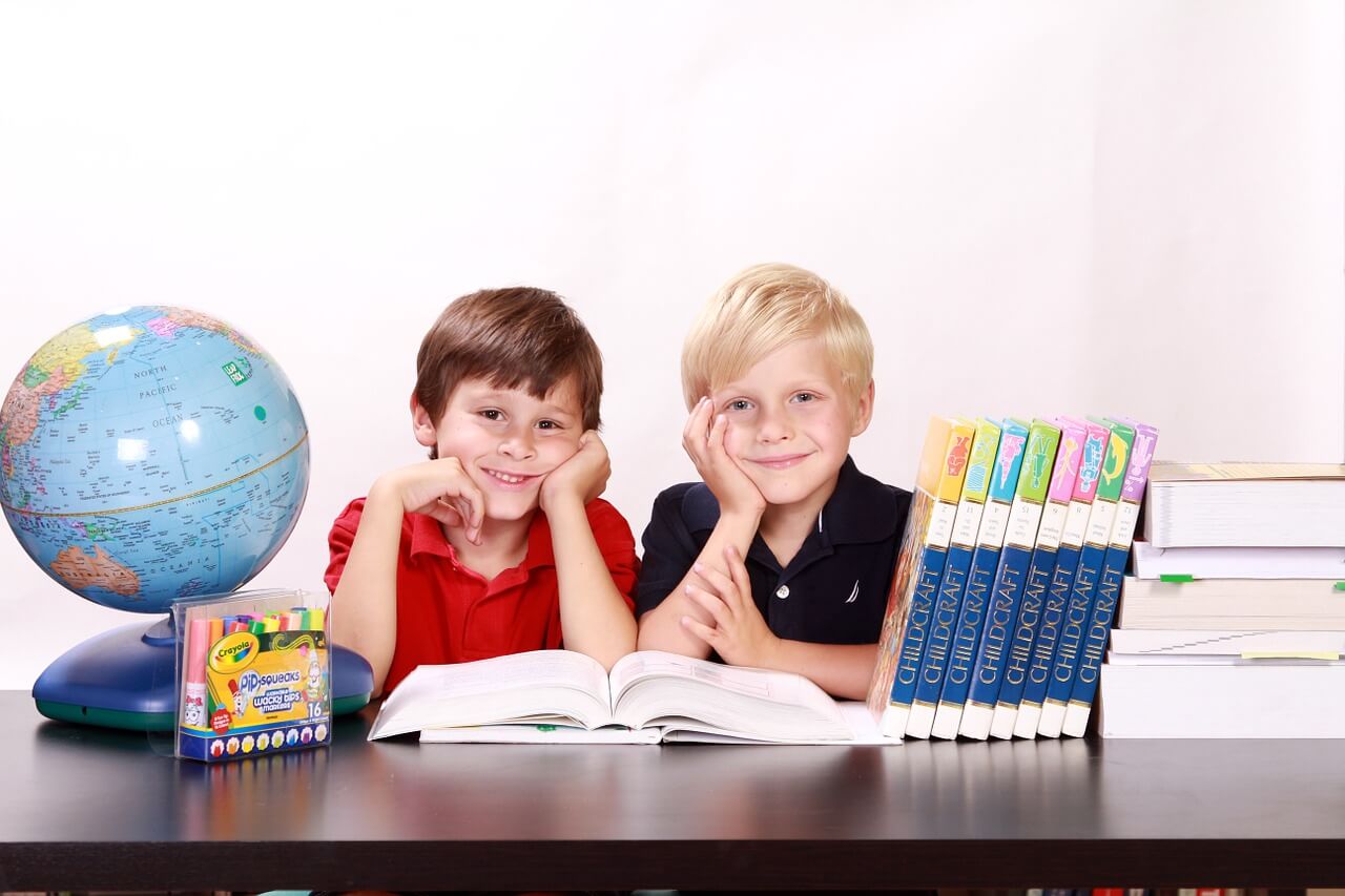 Two kids sitting at a desk with educational materials