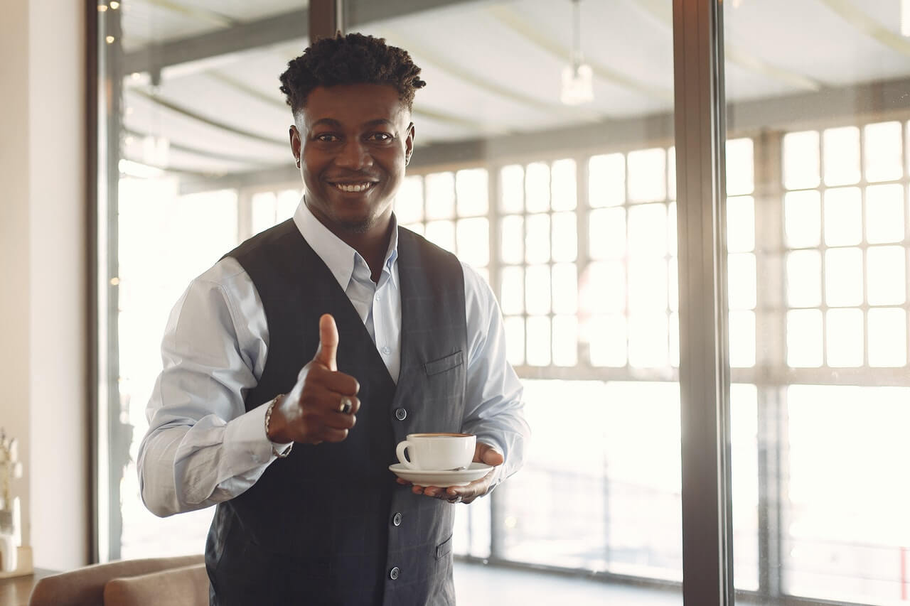Smiling business man with coffee gesturing thumbs up to a staff