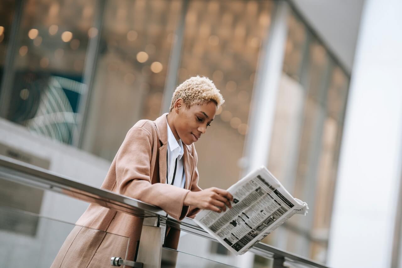 Young woman reading newspaper outside