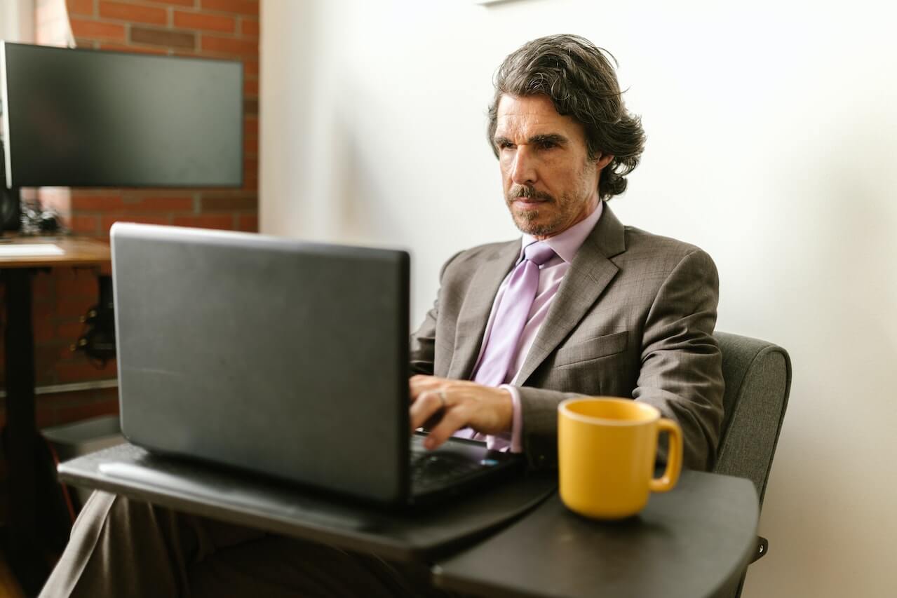 A man wearing grey suit typing on his laptop