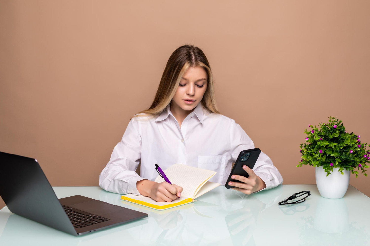 Young-business woman-using a-phone-while-writing on a notebook