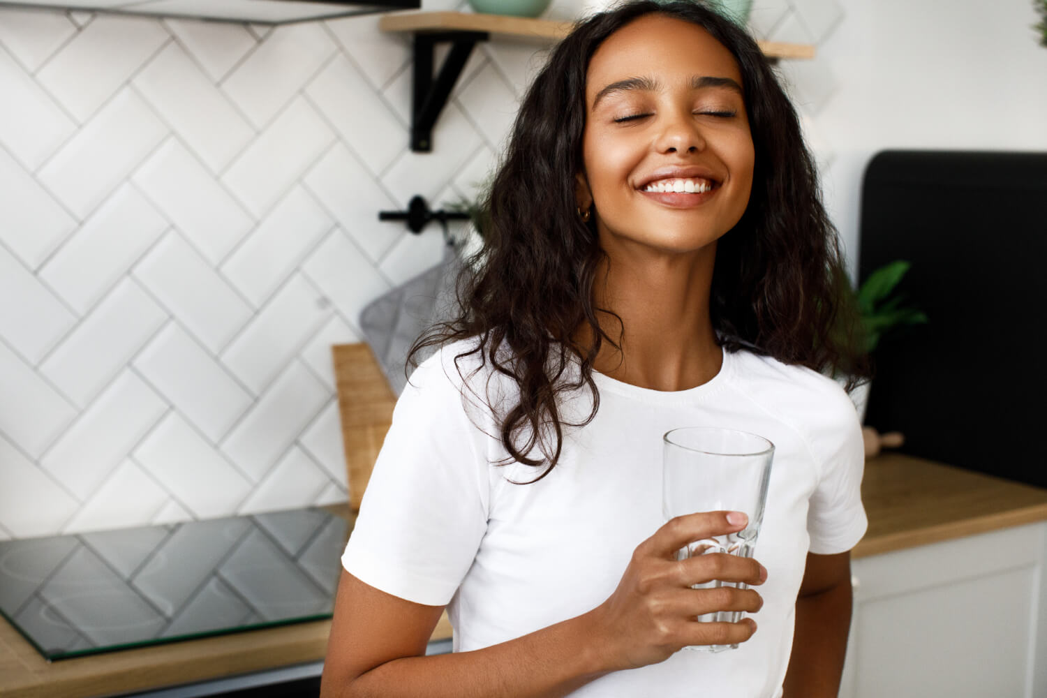 A lady smiling and holding a glass of water in her hand