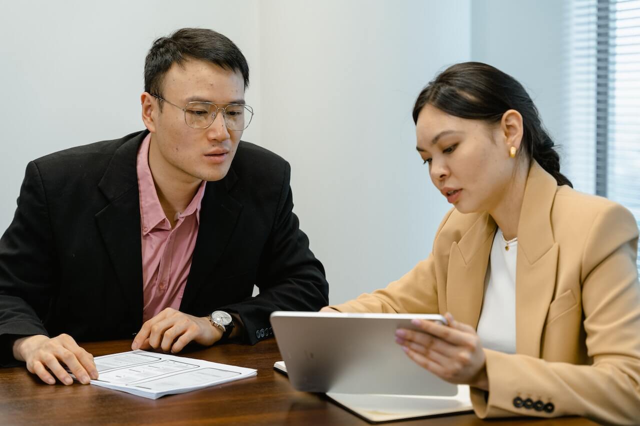 Business lady questioning a man seated looking at the tab screen